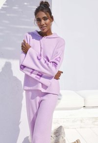 Set di felpa e pantaloni abbinati in lilla, realizzato in tessuto morbido, con maniche oversize e una tasca frontale a marsupio. Design testuale sulle maniche.