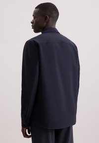 Granatowa koszula o prostym kroju, z długimi rękawami, mankietami na guziki i wykładanym kołnierzykiem. Gładki materiał o delikatnym połysku, bez widocznych wzorów.