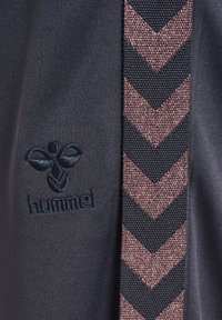 Ciemna tkanina z haftowanym czarnym logo hummel oraz pionowym, teksturowanym paskiem z różowo-czarnym wzorem w jodełkę.