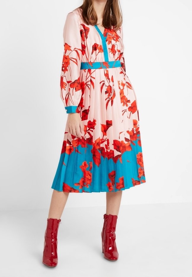 Blumenkleid mit langen Ärmeln, pinkfarbener Stoff mit roten Blumen, türkisfarbenen Akzenten, gefälteltem Rock, kombiniert mit glänzenden roten Stiefeletten.