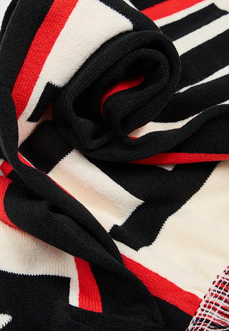 Dzianina w rolkach z dużymi czarno-białymi paskami i czerwonymi akcentami, tworząca teksturowany wygląd. Miękki materiał, lekka konstrukcja.