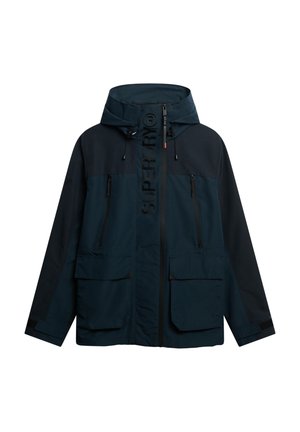 Chaqueta impermeable azul marino con cierre frontal, capucha ajustable y múltiples bolsillos con cremallera. Presenta el logo "SUPERDRY" en el pecho.
