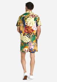 Short-sleeve button-up shirt and shorts set in bright, multicolored tropical patterns with large leaves, flowers, and animal prints.