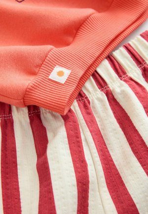 Korallfarbener Sweatshirt mit gerippten Bündchen, kombiniert mit leichten, dehnbaren, gestreiften Shorts in Creme und Rot mit einem elastischen Bund.