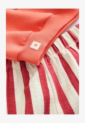 Hanorac corai cu manșete ribbed, asociat cu pantaloni scurți ușori și elastici cu dungi în crem și roșu, având un tiv elastic.