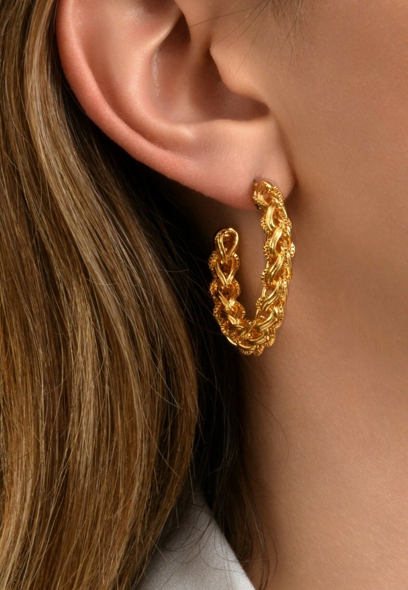 Boucle d'oreille en or avec un design tressé et des détails texturés, présentée sur un fond de tons de cheveux et de peau.
