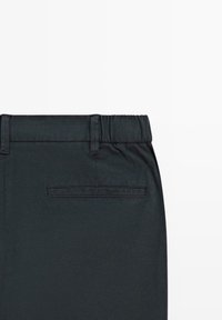 Zwarte stoffen broek met een elastische tailleband en een enkele horizontale achterzak met stikseldetails.