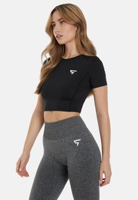 Čierne športové cropped tričko s krátkymi rukávmi a bielym logom, v kombinácii s vysokými šedými legínami s rovnakým logom.