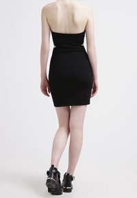 Černé bezramínkové šaty se slim siluetou, s vytočeným detailem v pase a strukturovanou tkaninou. V kombinaci s černými platformovými botami.