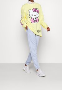 Camisa amarilla de manga larga con un gran gráfico de Hello Kitty, combinada con pantalones de chándal azul claro y zapatillas blancas.