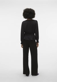 Haut à manches longues noir avec une taille froncée, associé à un pantalon noir à jambes larges. L'ensemble présente un tissu texturé et une silhouette décontractée.