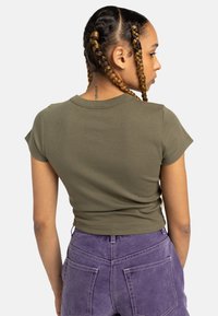 Olivové rebrované crop top s krátkymi rukávmi, ktorý má okrúhly výstrih a priliehavý strih, skombinovaný s fialovými nohavicami s vysokým pásom.