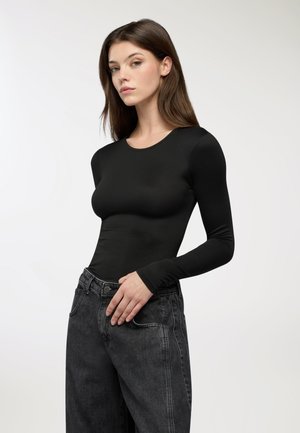 Top nero a maniche lunghe in tessuto morbido, con scollatura rotonda. Abbinato a jeans in denim scuro a vita alta con un leggero lavaggio.