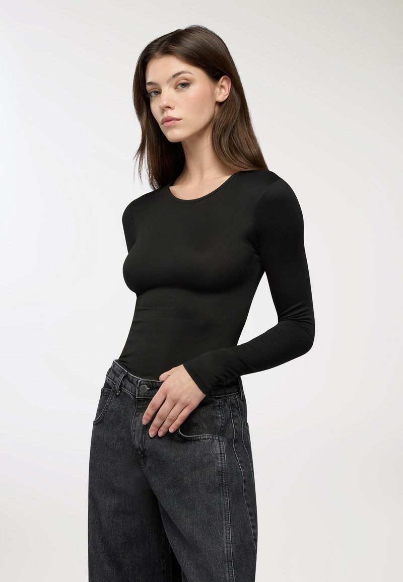 Czarna bluzka z długimi rękawami z gładkiego materiału, z okrągłym dekoltem. Połączona z ciemnoniebieskimi dżinsami o wysokim stanie z delikatnym przetarciem.