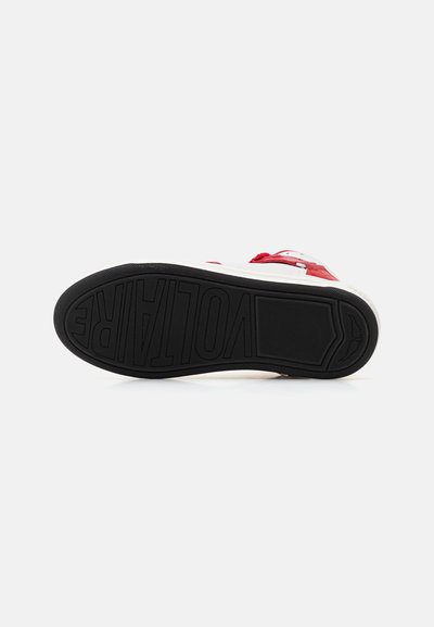 Red and white sneaker with a textured black rubber sole featuring "VOLTARE" embossed. The heel shows a contrasting color accent.