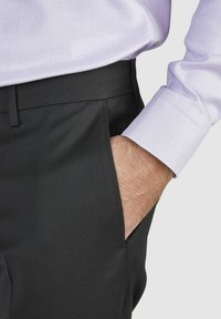 Schwarze Hose aus glattem Stoff mit einer Seitentasche, kombiniert mit einem helllila strukturierten Hemd. Sichtbare Manschettendetails.