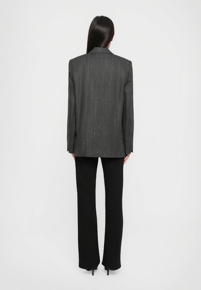 Blazer grigio con strisce verticali bianche, vestibilità su misura e rever a punta, abbinato a pantaloni neri a zampa d'elefante e décolleté.