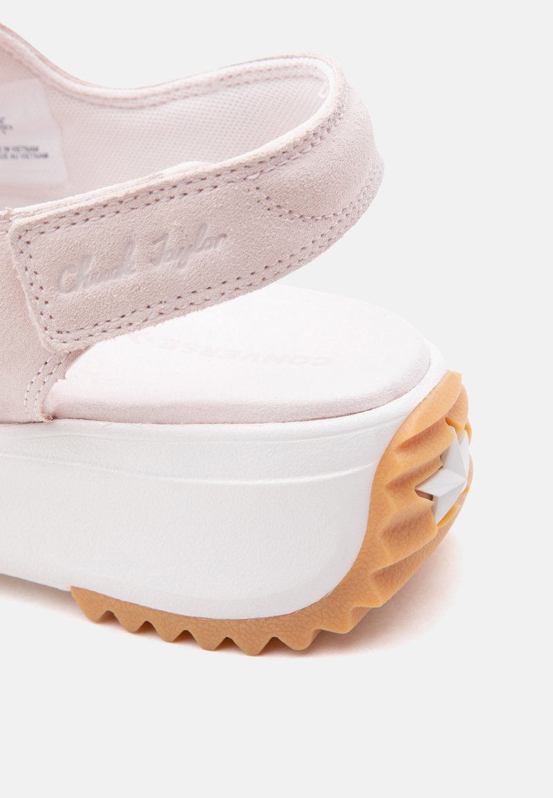 Cinturino in camoscio rosa chiaro con testo in rilievo "Chuck Taylor", attaccato a una spessa suola piatta bianca con suola di gomma scanalata e dettaglio a stella.