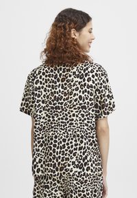 Košile s krátkým rukávem v leopardím vzoru s černými skvrnami na béžovém pozadí. Volný střih, měkká textura, ležérní design.