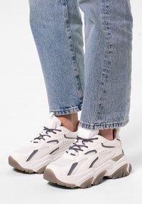 Chaussures : baskets blanches épaisses avec des accents gris, en matériaux en mesh et synthétiques, semelles texturées et talons en caoutchouc épais. Portées avec un jean bleu retroussé.