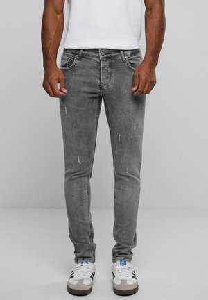 Gray denim jeans with distressed detailing, slim fit, five pockets, and a zip fly. Worn with white and grey sneakers.