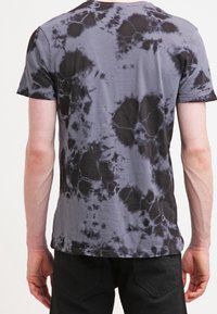 Šedé tričko s tie-dye vzorem, kulatým výstřihem a krátkými rukávy. Vzorek obsahuje tmavé černé skvrny na světle šedém pozadí.