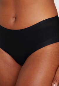 Black brief made from smooth fabric, featuring a seamless design and wide waistband, emphasizing comfort and fit.