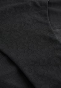 Tela negra con una textura sutil de estampado de leopardo; combina texturas lisas y tipo malla con patrones variados y diferentes profundidades en la superficie.