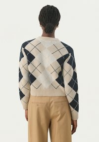 Sweter w kolorze kremowym i granatowym w wzór argyle z prążkowanymi mankietami i dolnym wykończeniem, zawierający geometryczne kształty oraz luźny krój. Zobrazowane z tyłu.