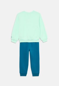 Mäkký mintový sveter so rebrovaným okrúhlym výstrihom a manžetami, spod ktorého sú tmavozelené teplákové nohavice s elastickými manžetami. Vyrobené z jemnej bavlny.