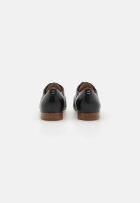 Black leather shoes with a rounded toe, low wooden heel, and a smooth texture. Features two decorative accents on the back heel.