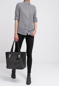 Camicia a quadri bianco e nero con bottoni, jeans skinny neri, stivaletti, e una grande borsa a tracolla nera con dettagli in borchie.