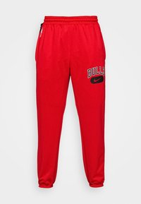Pantalones joggers rojos de algodón con cintura elástica, tobillos ajustados, impresión en negro de "BULLS" y el logo de Nike en el costado. Incluyen bolsillos laterales con cremallera.