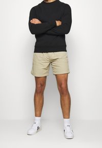 Černá mikina a béžové šortky s volným střihem. Bílé tenisky s černými akcenty. Minimalistický design a ležérní styl.