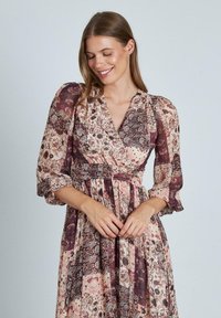 Lungo vestito floreale con scollatura a V profonda, maniche a sbuffo e vita elastica. Presenta un design a patchwork in tonalità di rosa, bordeaux e crema.