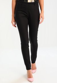 Sorte skræddersyede bukser med en slank pasform, der har en glat tekstur uden synlige mønstre eller hardware, kombineret med lyserøde hæle.