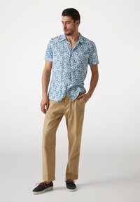 Camisa de manga corta y cuello con un patrón geométrico azul, combinada con pantalones beiges y zapatos azul oscuro con cordones marrones y suela blanca.