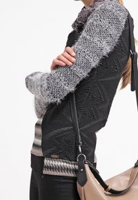 Pull en tricot noir et gris avec des motifs texturés, doté d'un col et de poignet côtelés ; accompagné d'un sac bandoulière beige.