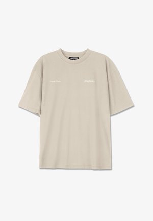 Világos bézs pamut póló rövid ujjal, kerek nyakkivágással, finoman fehér nyomtatott szöveggel az elején és laza szabással.