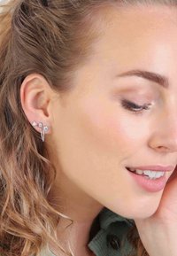 Zilverkleurige oorbellen met drie geometrische vormen: een driehoek, een ronde steen en een druppelvorm. Textuurdetail in de ketting verbindt ze.