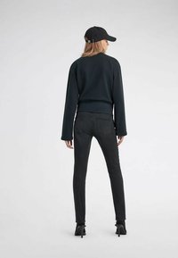 Felpa nera con maniche lunghe, orlo corto, abbinata a jeans skinny scuri e scarpe con tacco nere, modella che indossa un berretto nero.