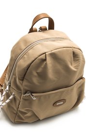 Mochila de tela color beige con forma redondeada, que incluye cremalleras plateadas, un bolsillo frontal y un detalle de cuero marrón con el logo.