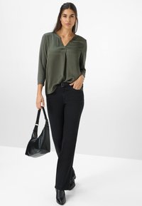 Mørkegrøn V-hals bluse med trekvartærmer, parret med sorte lige ben jeans. Holder en sort håndtaske, iført sorte ankelstøvler.