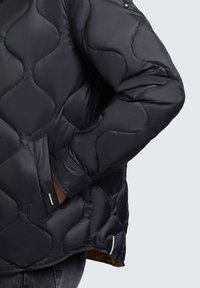 Sort polstret jakke med et quiltet mønster, der har en lynlåslomme og minimal branding. Glat tekstur og let glans.