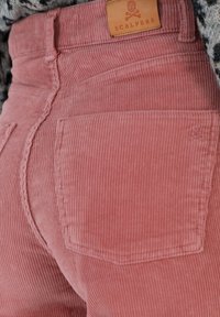 Roze corduroy broek met verticale ribbelstructuur, voorzien van een leren label met de tekst "SCALPERS" en twee achterzakken.