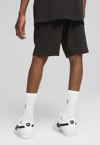 Shorts en coton noirs avec une coupe décontractée, associés à des chaussettes blanches montant jusqu'à la cheville avec un logo noir, et des baskets blanches avec des accents noirs.