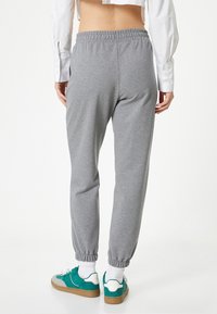 Pantalones jogger de algodón gris con cintura y puños elásticos, que cuentan con un corte relajado. Combinados con zapatillas en tonos azul verdoso y blanco.