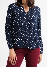 Blouse bleu marine avec des pois blancs, manches longues, devant boutonné et ourlet arrondi. Tissu léger avec une coupe décontractée.