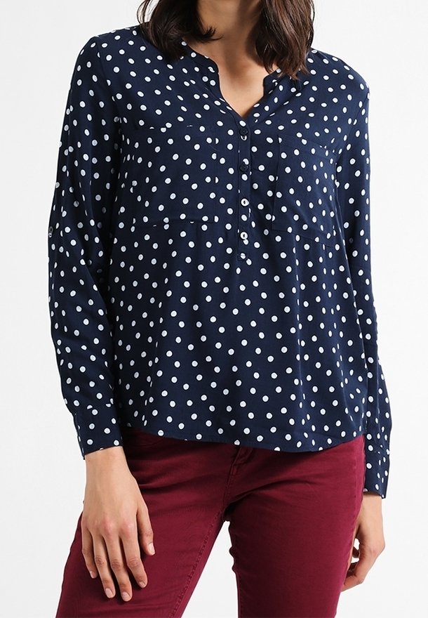Blouse bleu marine avec des pois blancs, manches longues, devant boutonné et ourlet arrondi. Tissu léger avec une coupe décontractée.