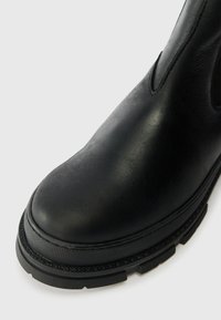 Bottines en cuir noir avec un bout rond, un panneau latéral élastique et une semelle en caoutchouc texturée. Le design met en avant la douceur et la durabilité.